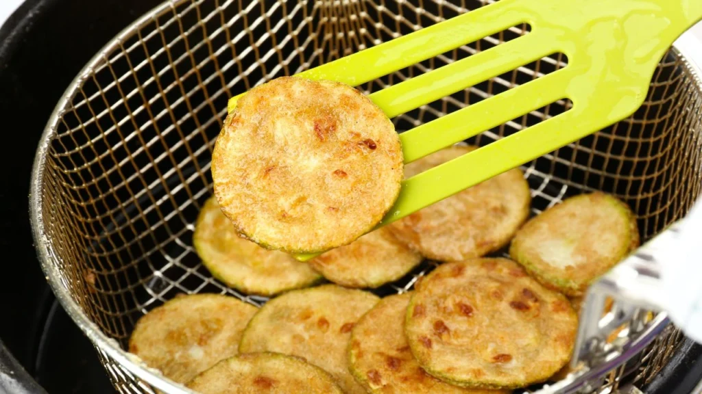 Cooked zucchini slices in a frying basket.