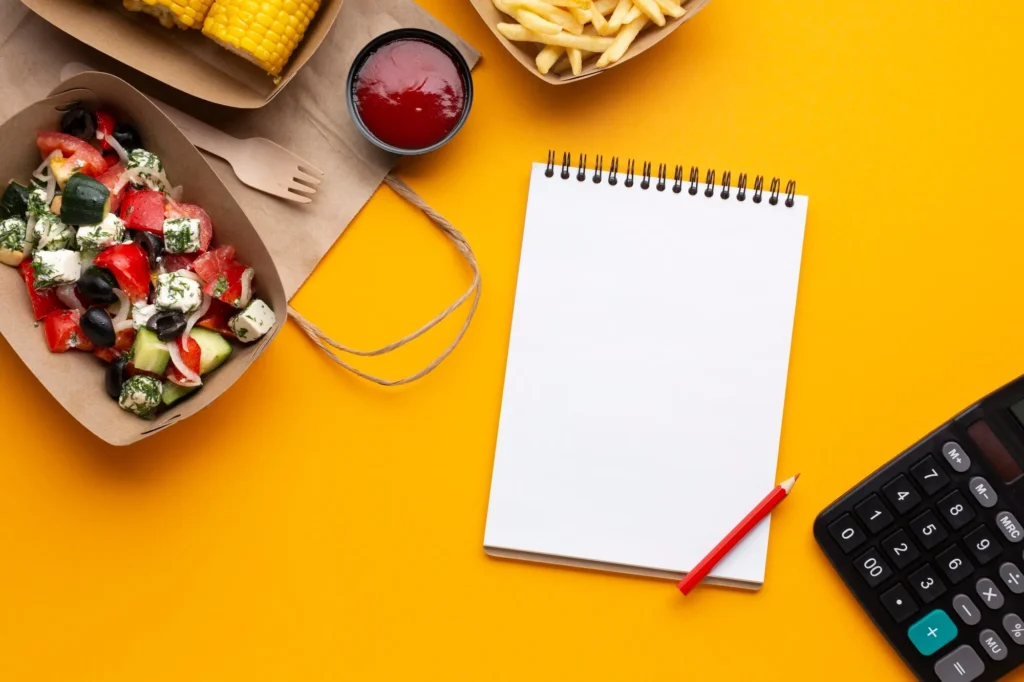 Notebook and calculator beside takeout food and salad