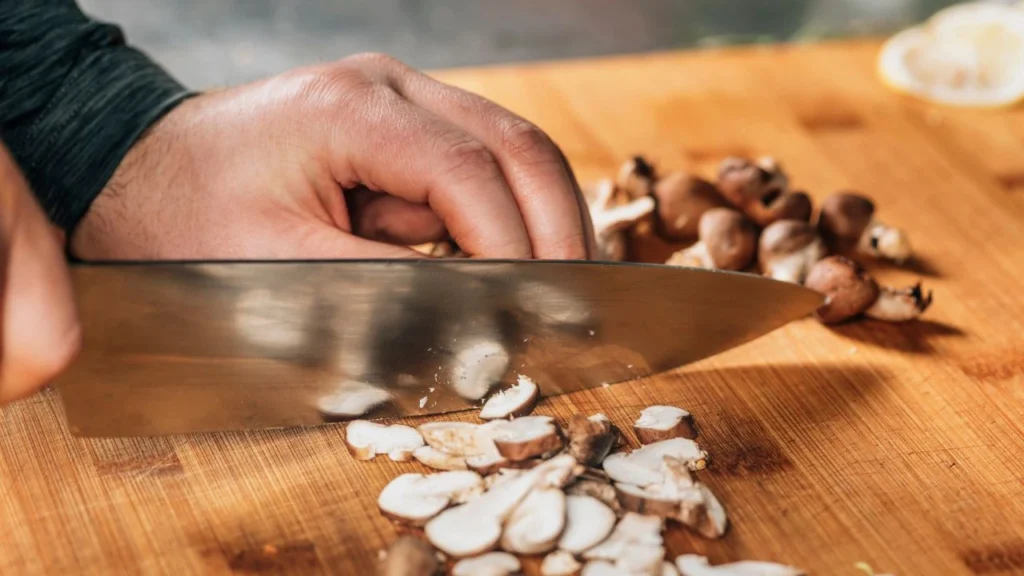  a chef slicing mushrooms on a wooden cutting board