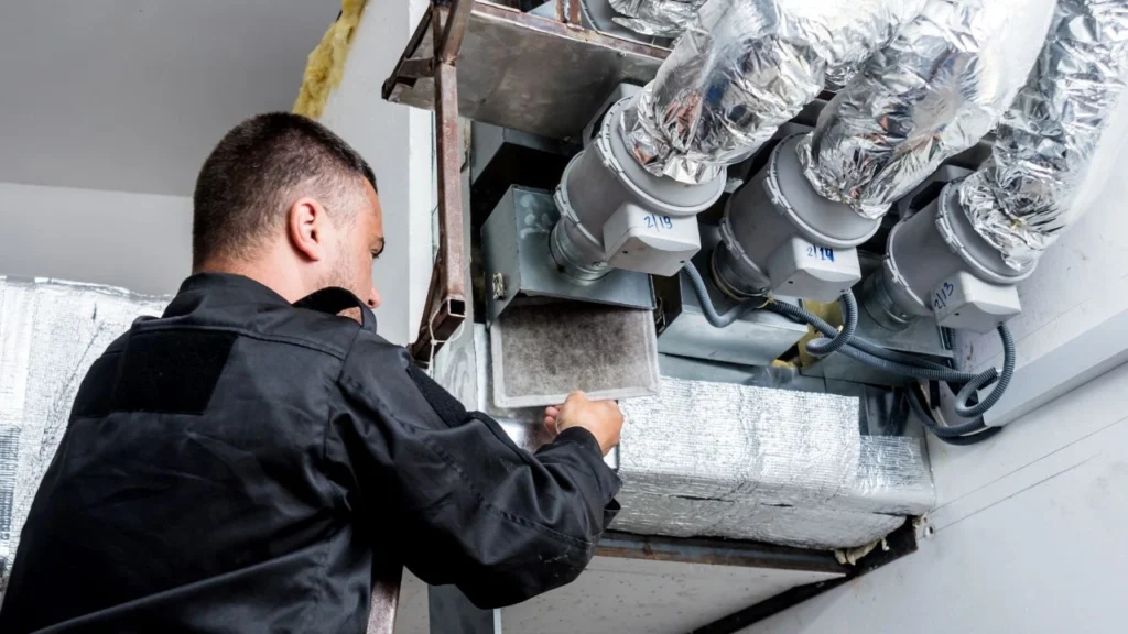 Worker inspecting a complex kitchen ventilation system with ducts and fans.