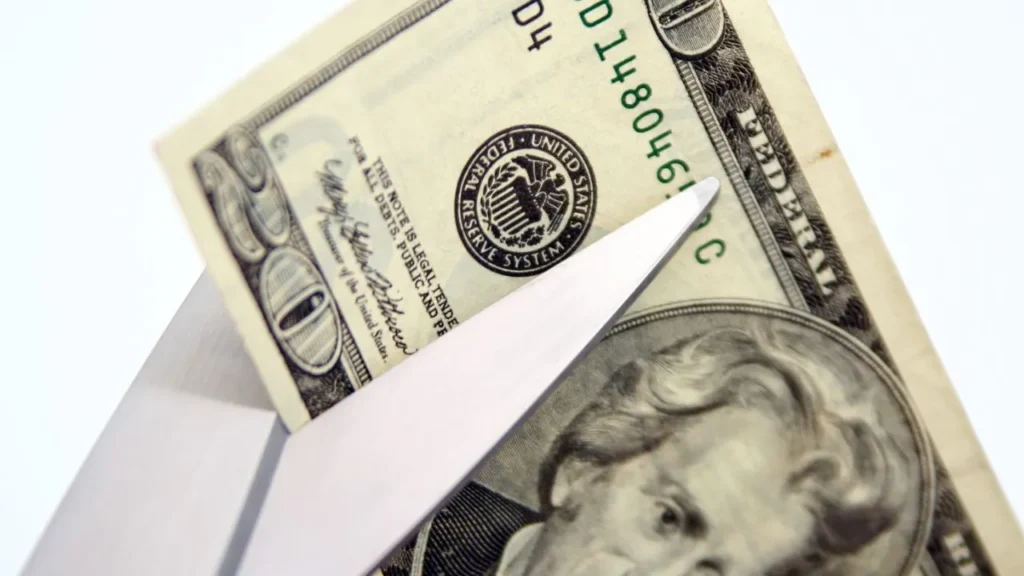 Scissors cutting a twenty dollar bill, symbolizing savings
