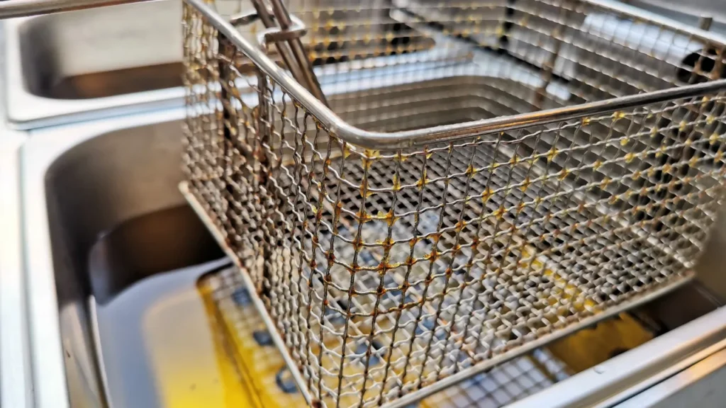 Metal fryer basket in oil-filled deep fryer.