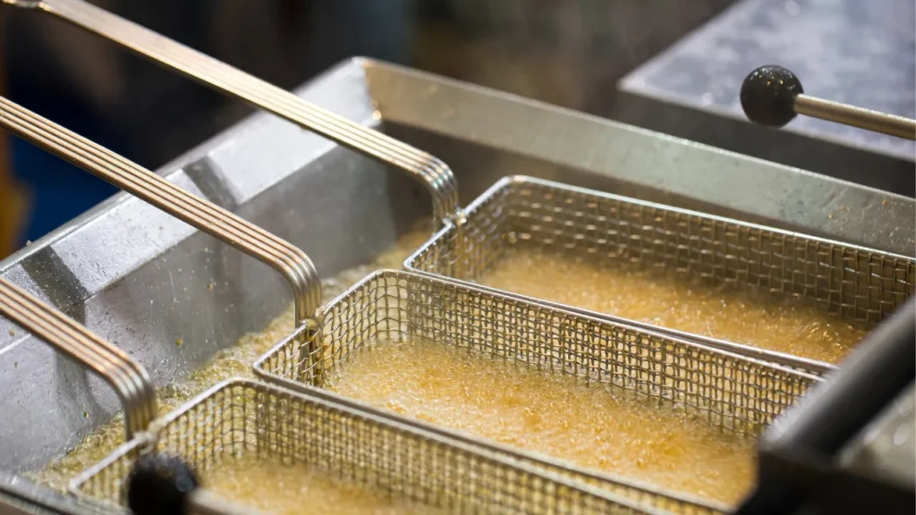 Deep fryer basket filled with hot bubbling oil, showcasing the process of frying food in a commercial kitchen setting.
