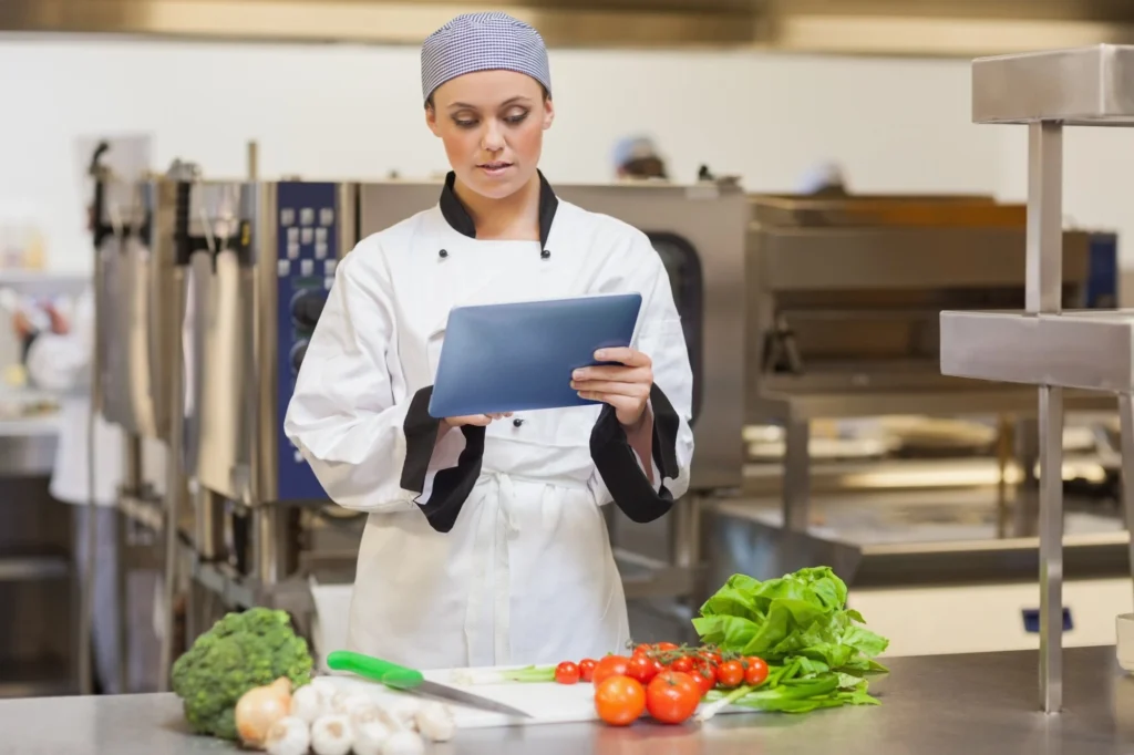 Female chef analyzing tablet with fresh ingredients.