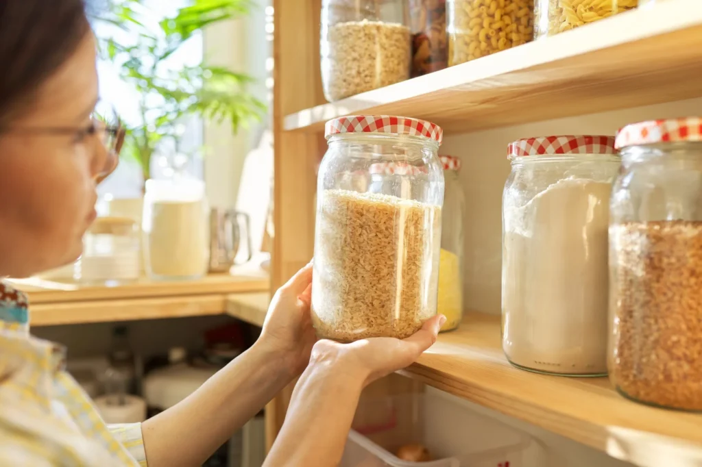 Dry goods stored in clear containers on wooden pantry shelves.