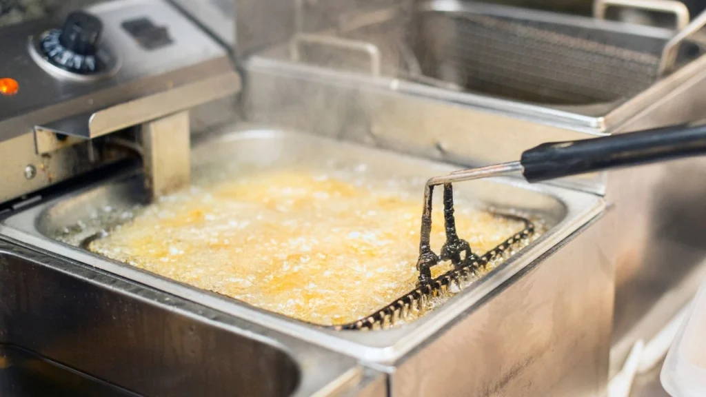 Commercial deep fryer with bubbling oil and a fryer basket handle.