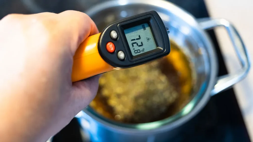 Hand holding digital thermometer measuring fry-oil temperature.