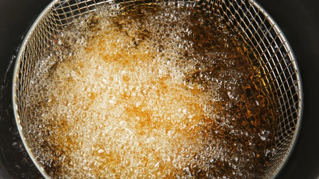 Close-up of bubbling oil in a deep fryer basket.