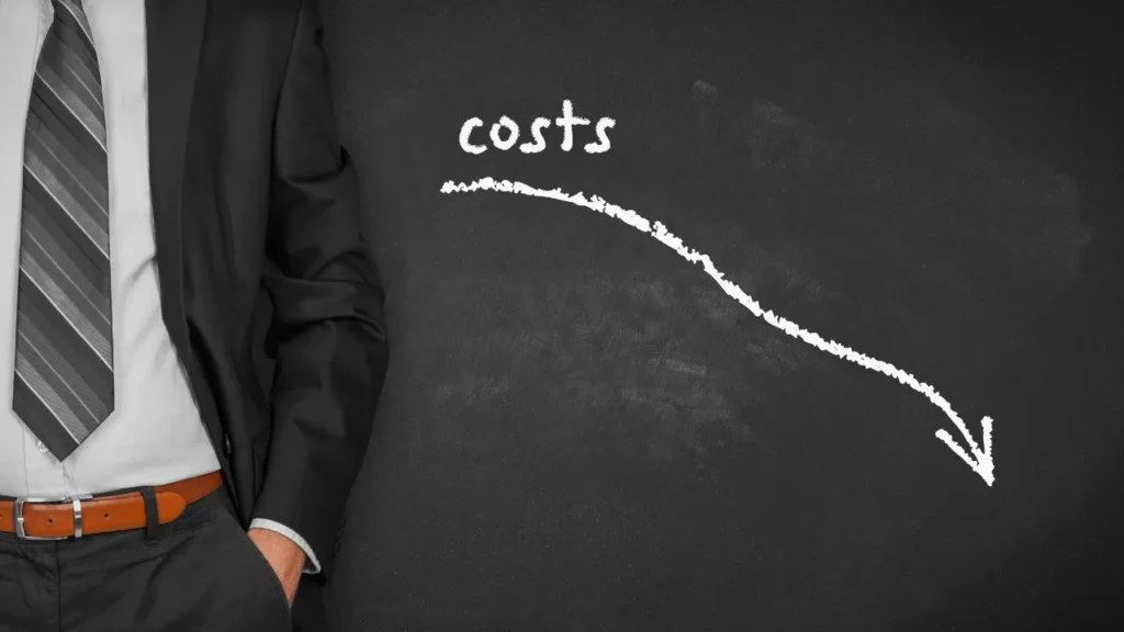 Businessman standing beside chalkboard with declining costs graph.