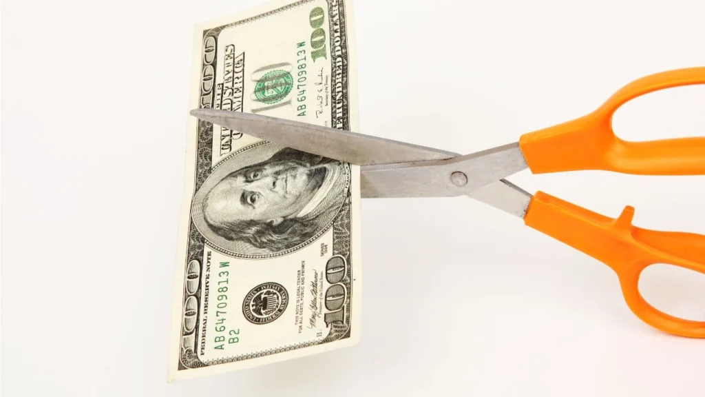 Scissors with orange handle cutting $100 USD