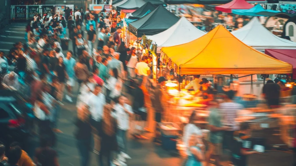 Busy outdoor market with colorful tents and people.