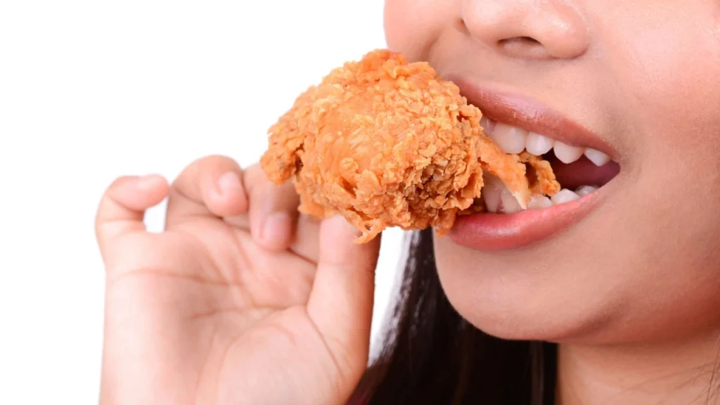 Person enjoying crispy fried chicken drumstick close up
