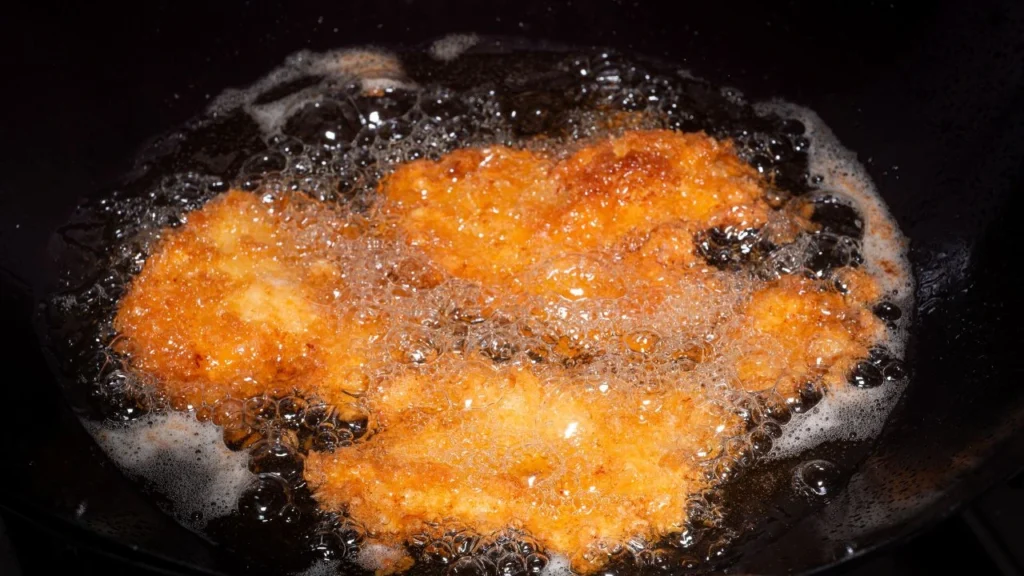 Breaded fried chicken in boiling oil in a Chinese wok.