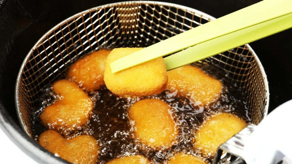 Golden nuggets frying in oil with green tongs lifting one.