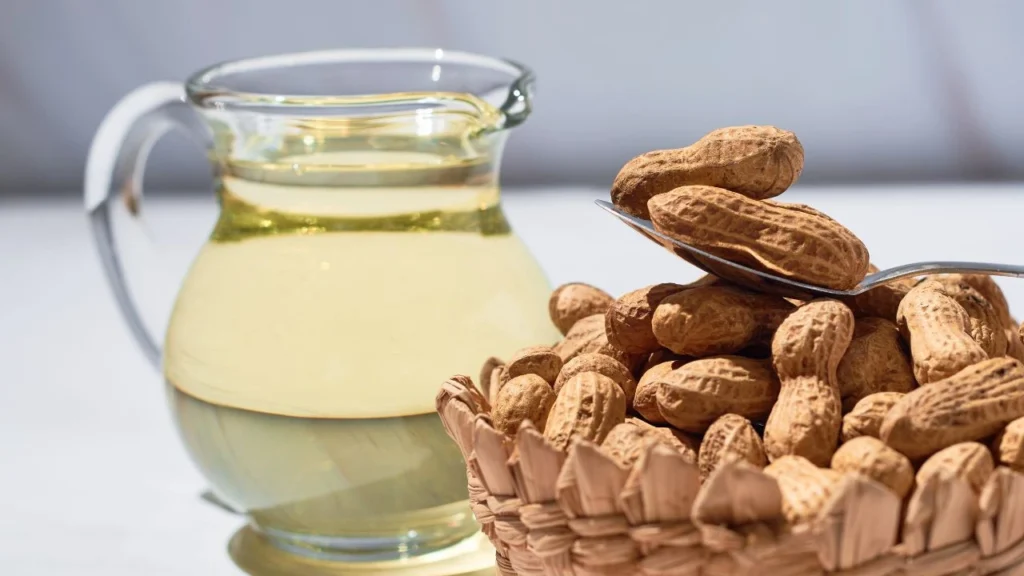 Glass jug of peanut oil with basket of whole peanuts.