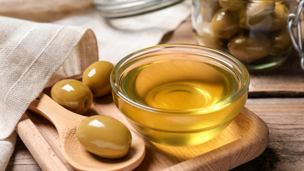 bowl of cooking oil with green olives on wood block