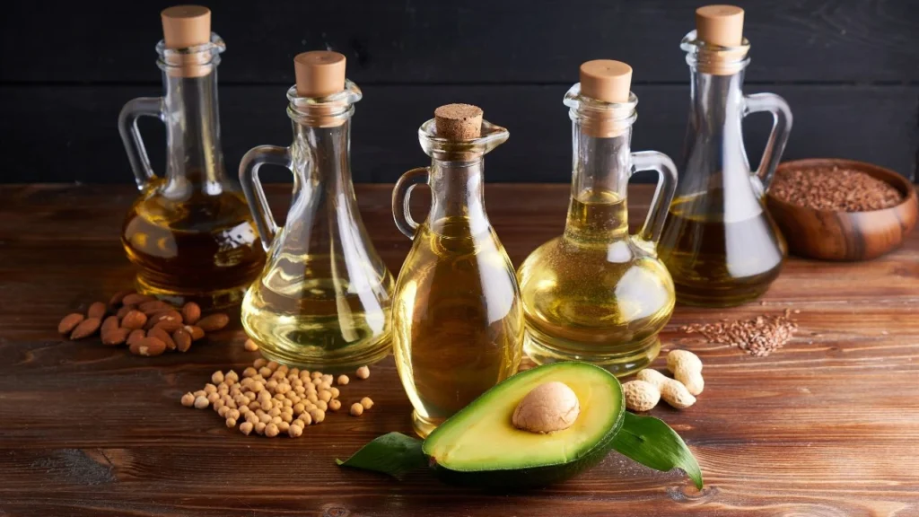 Assorted glass bottles of oils with avocado and nuts displayed.
