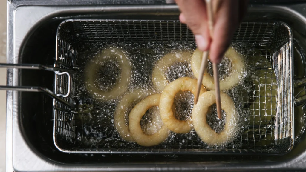 Person’s hand frying onion rings