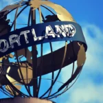 Metal globe sculpture with 'Portland' sign against blue sky near northwest food show.