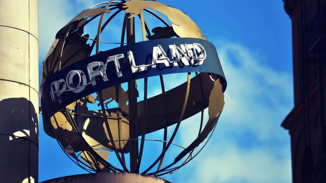 Metal globe sculpture with 'Portland' sign against blue sky near northwest food show.