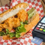 Fried chicken sandwich with lettuce and tomato next to a payment terminal, representing types of POS systems for food trucks.