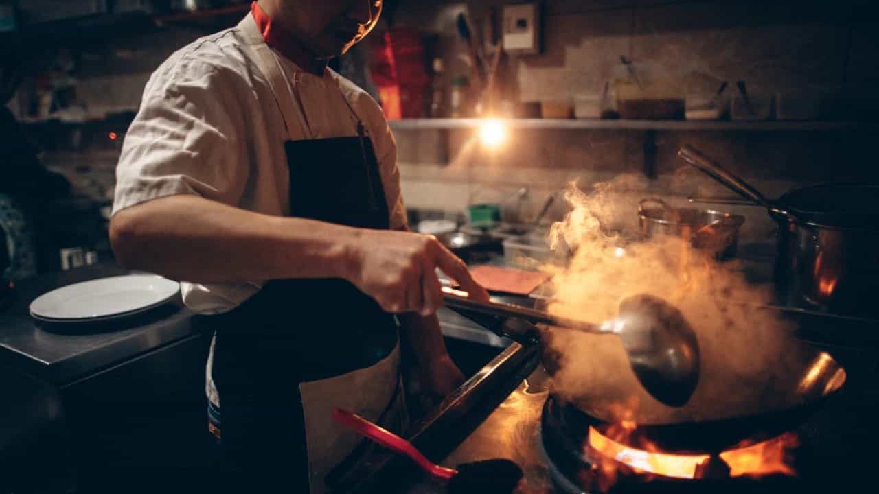 Chef cooking with steam in a hot kitchen.