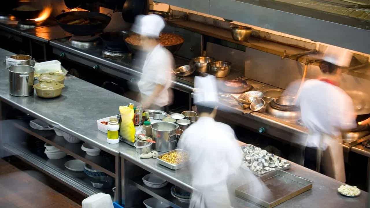 Busy commercial kitchen with chefs preparing multiple dishes.