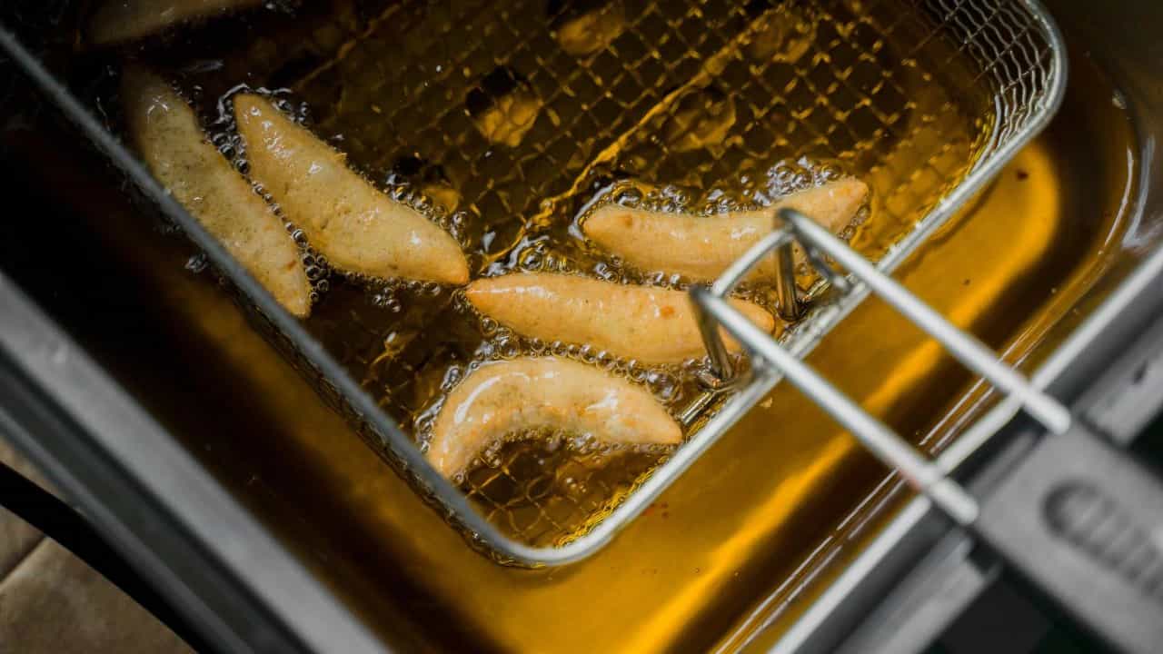 Golden fried food cooking in a commercial deep fryer basket.
